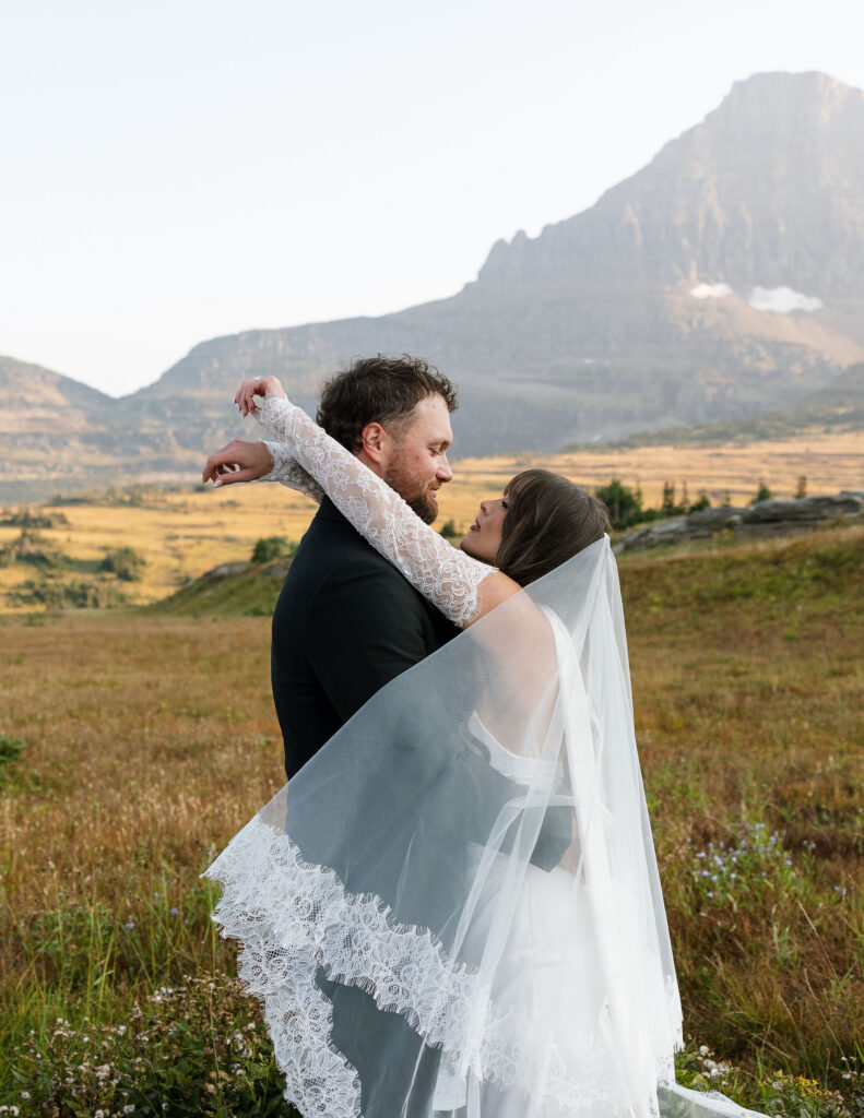 Bride and groom embracing with mountain peaks behind them during a Glacier National Park elopement