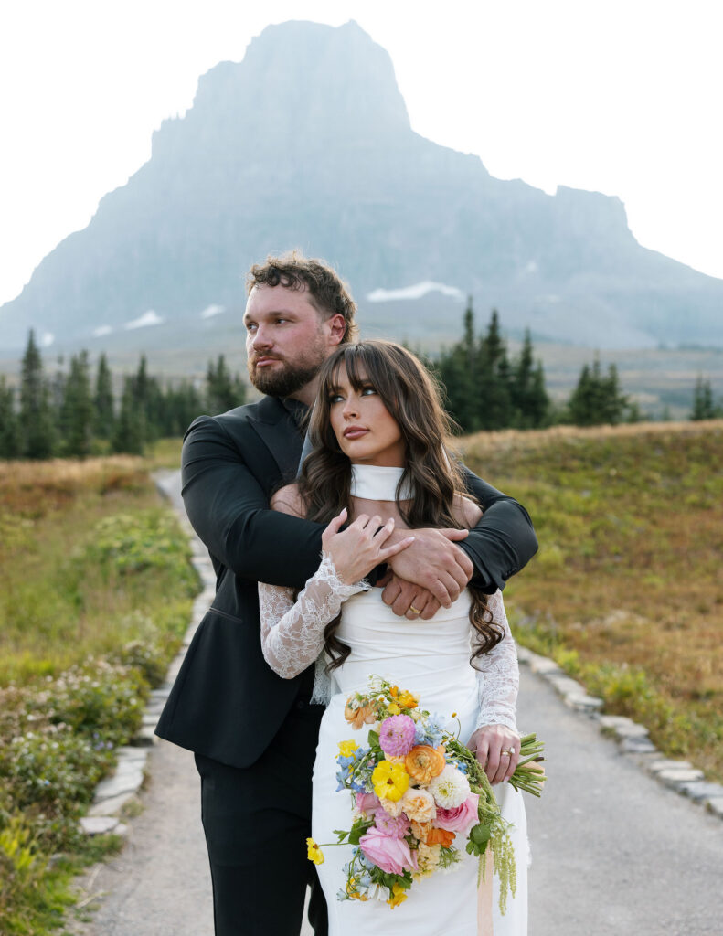 Bride and groom embracing with a mountain peak behind them during a Glacier National Park elopement