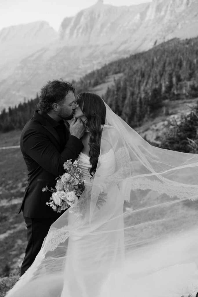 Black and white portrait of bride and groom kissing with veil flowing during a Glacier National Park elopement