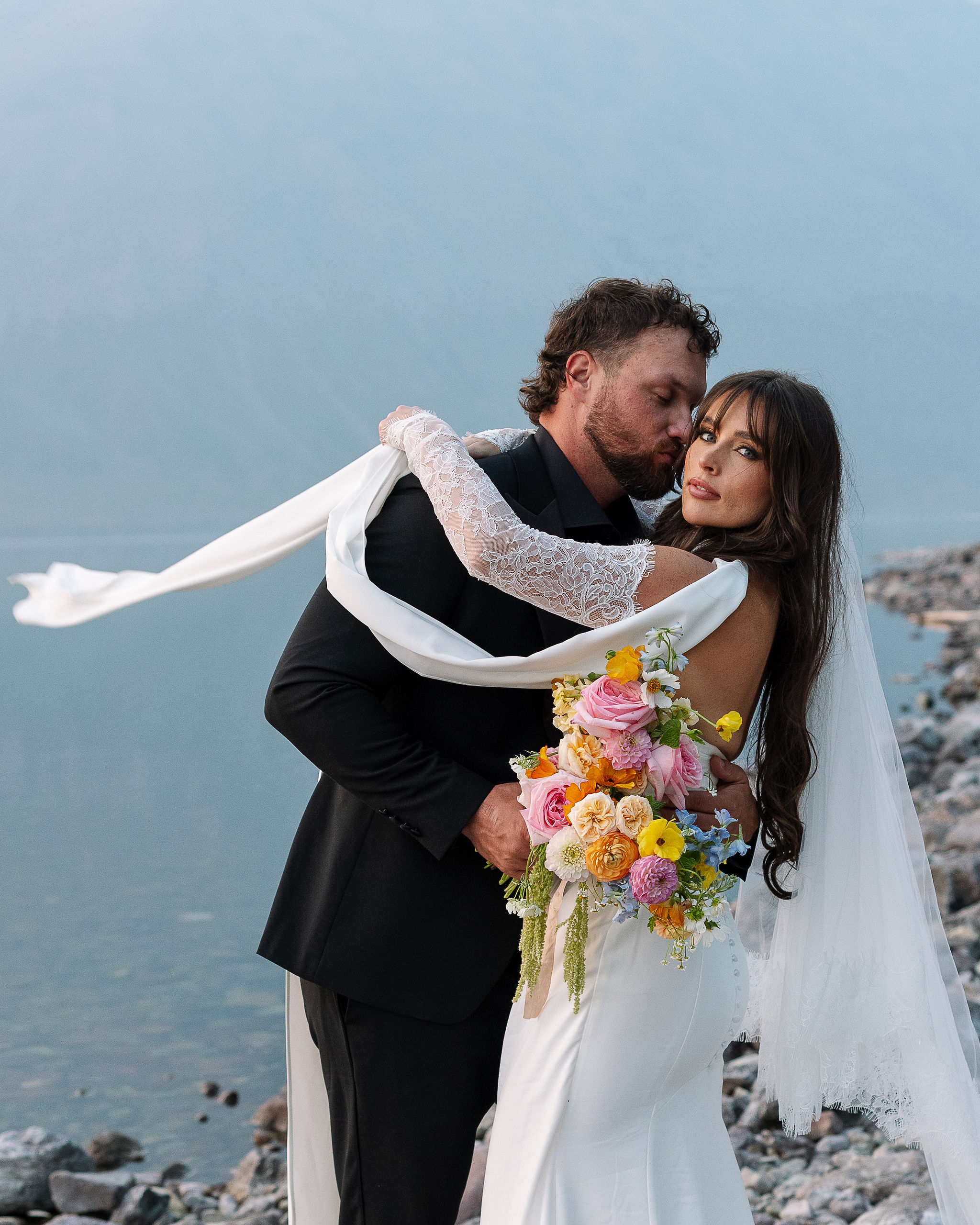 Couple embracing with a flowing veil and colorful bouquet during a Glacier National Park elopement