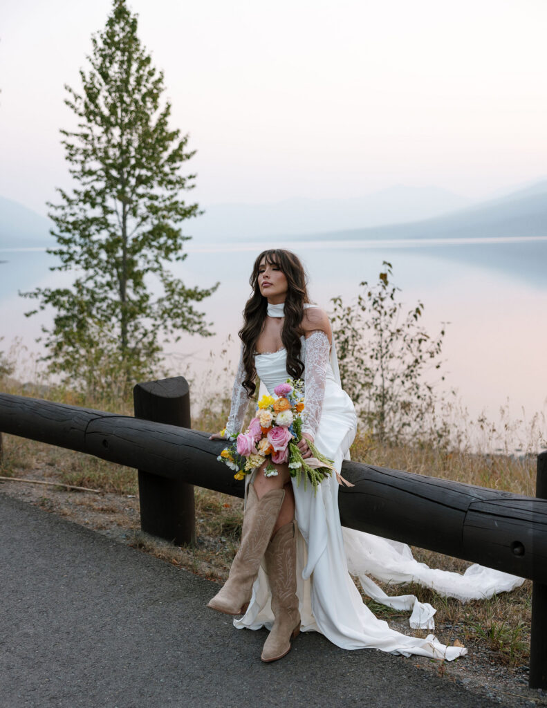 Bride standing beside a scenic road overlooking a glacial lake in Glacier National Park holding her bouquet