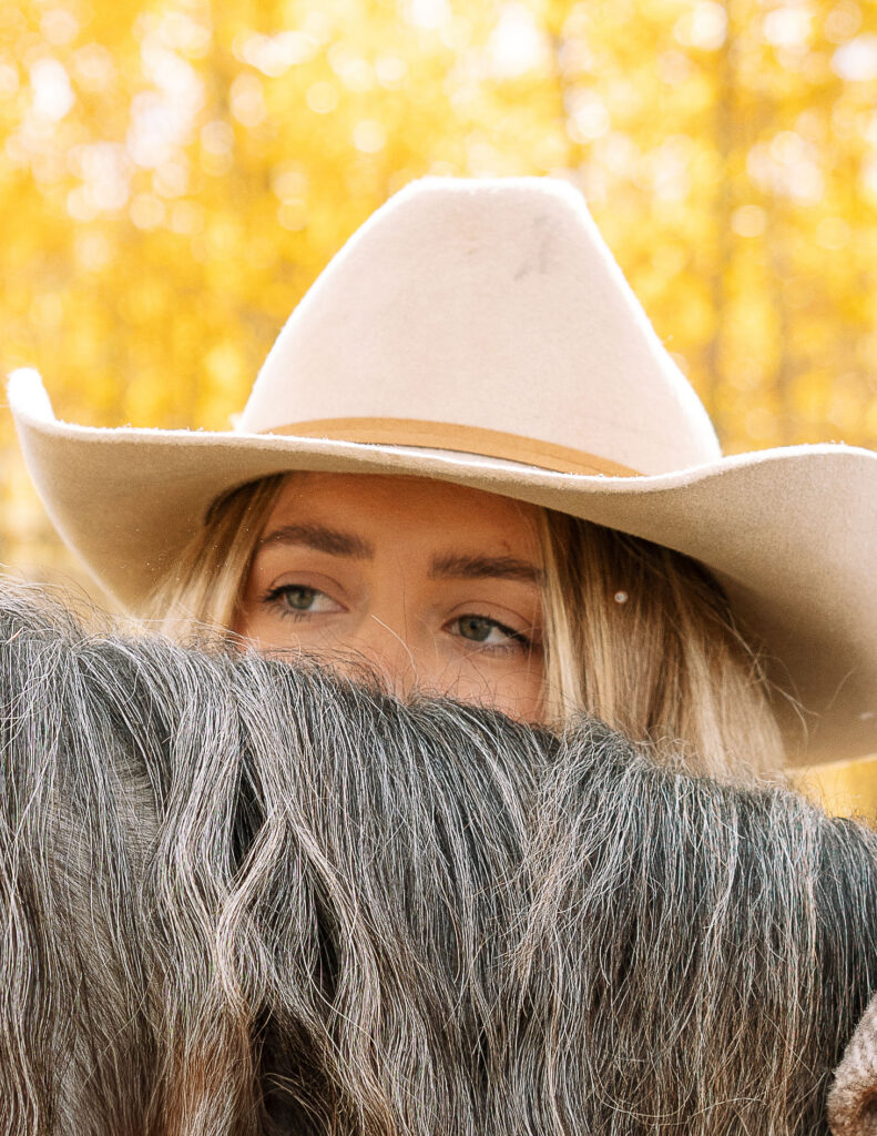 Close-up of a Haley Jessat wearing a tan cowboy hat standing beside a gray horse during a western lifestyle photoshoot in Montana