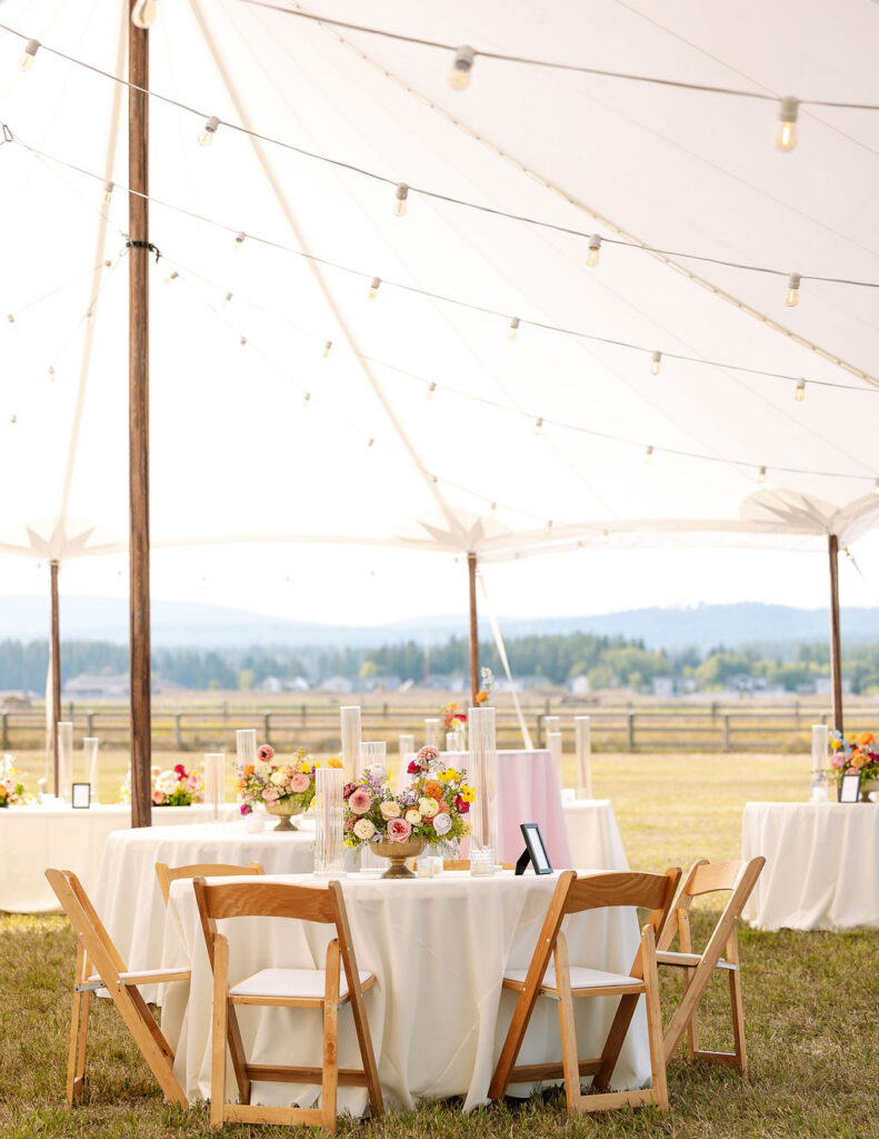 Reception tables set inside a tent with string lights and mountain views during a summer wedding in Whitefish Montana