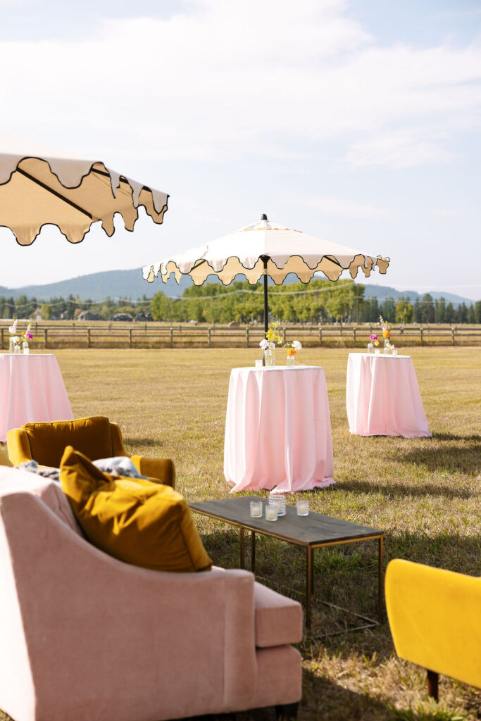 Outdoor cocktail tables with pink linens and mountain views during a summer wedding reception in Whitefish Montana