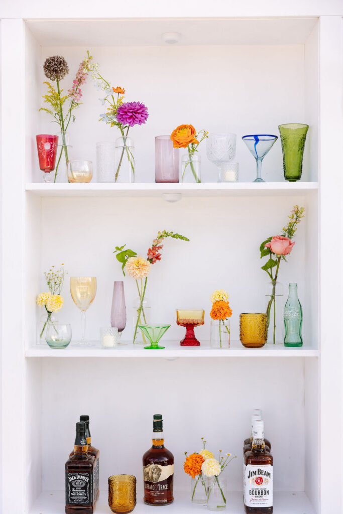 Shelving display with colorful glassware and floral arrangements used as wedding reception decor