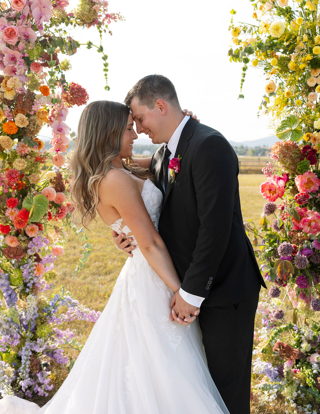 Bride and groom standing together beneath a colorful floral ceremony installation during sunset portraits in Whitefish Montana