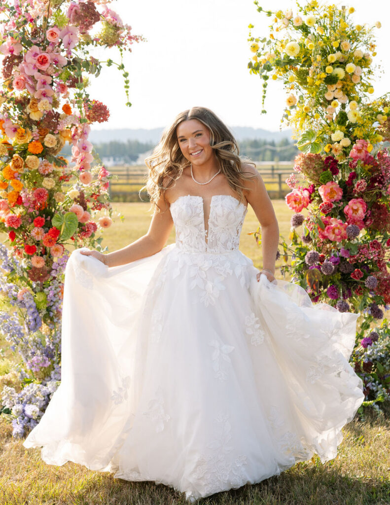 Bride standing beneath a colorful floral ceremony arch during golden hour portraits at a summer wedding in Whitefish Montana