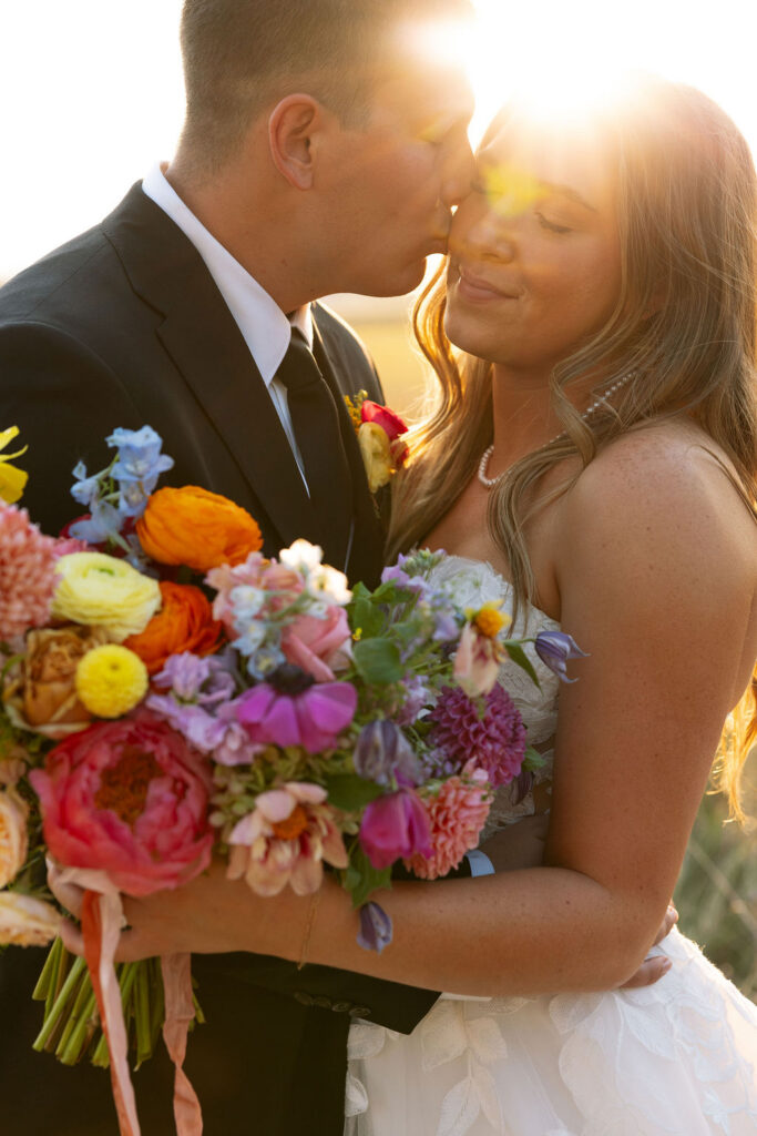 Close-up of bride holding a colorful bouquet while standing with groom during sunset wedding portraits in Whitefish Montana