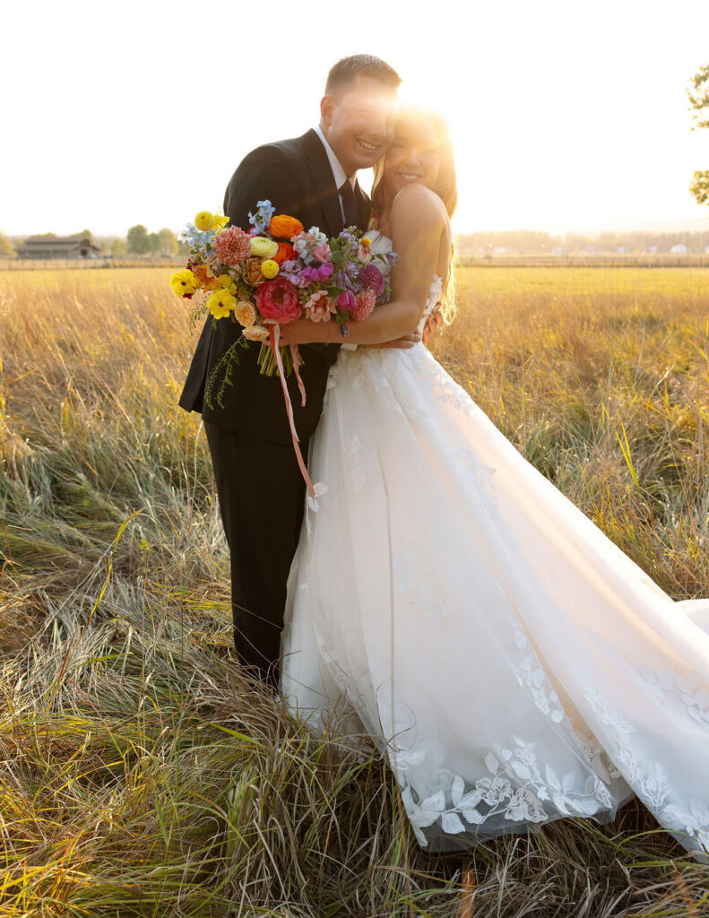 Bride and groom standing in tall grass with a colorful bouquet during golden hour wedding portraits in Whitefish Montana