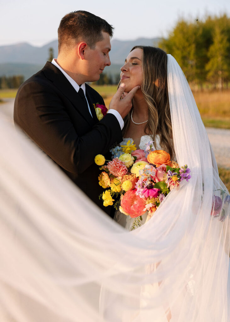 Bride and groom embracing under the bride’s veil while holding a vibrant bouquet during golden hour wedding portraits in Whitefish Montana