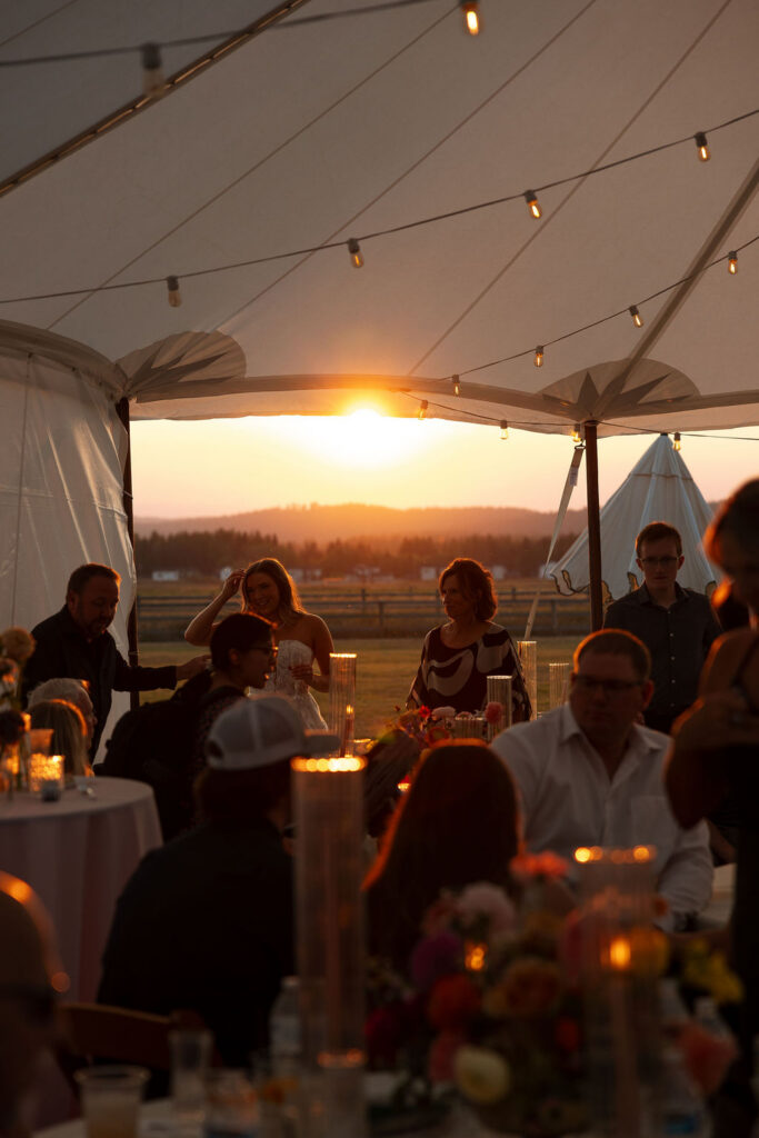 Guests seated inside a reception tent watching the sunset during a summer wedding celebration in Whitefish Montana