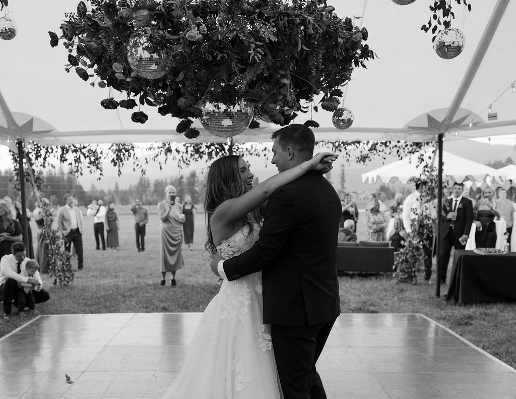 Bride and groom sharing their first dance under a floral installation during an outdoor wedding reception in Whitefish Montana