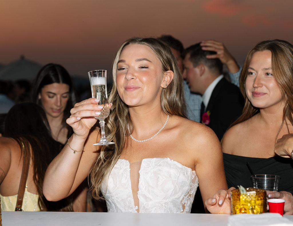 Bride in a strapless wedding dress holding a champagne glass and celebrating with friends during an outdoor summer wedding reception in Whitefish Montana