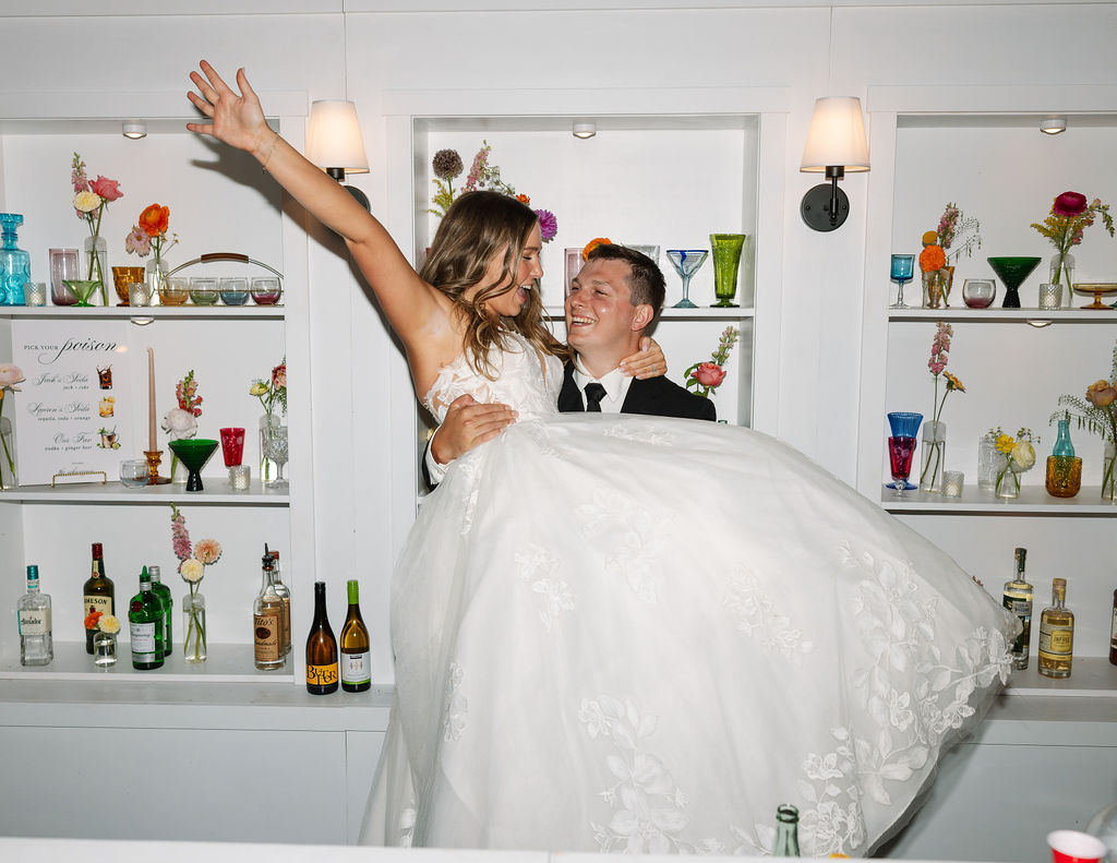 Bride being lifted by the groom while celebrating behind a bar during a fun wedding reception moment in Whitefish Montana captured by Haley Jessat
