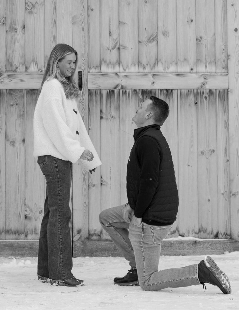 Black and white photo of man kneeling to propose during winter proposal in Whitefish Montana