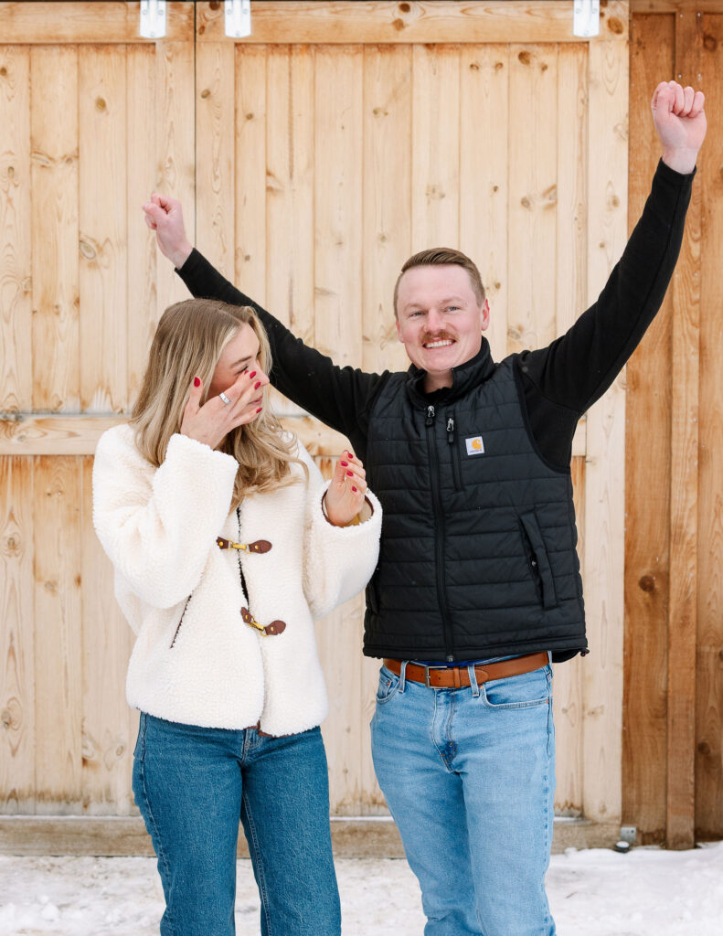 Couple celebrating engagement with raised arms after winter proposal in Whitefish Montana